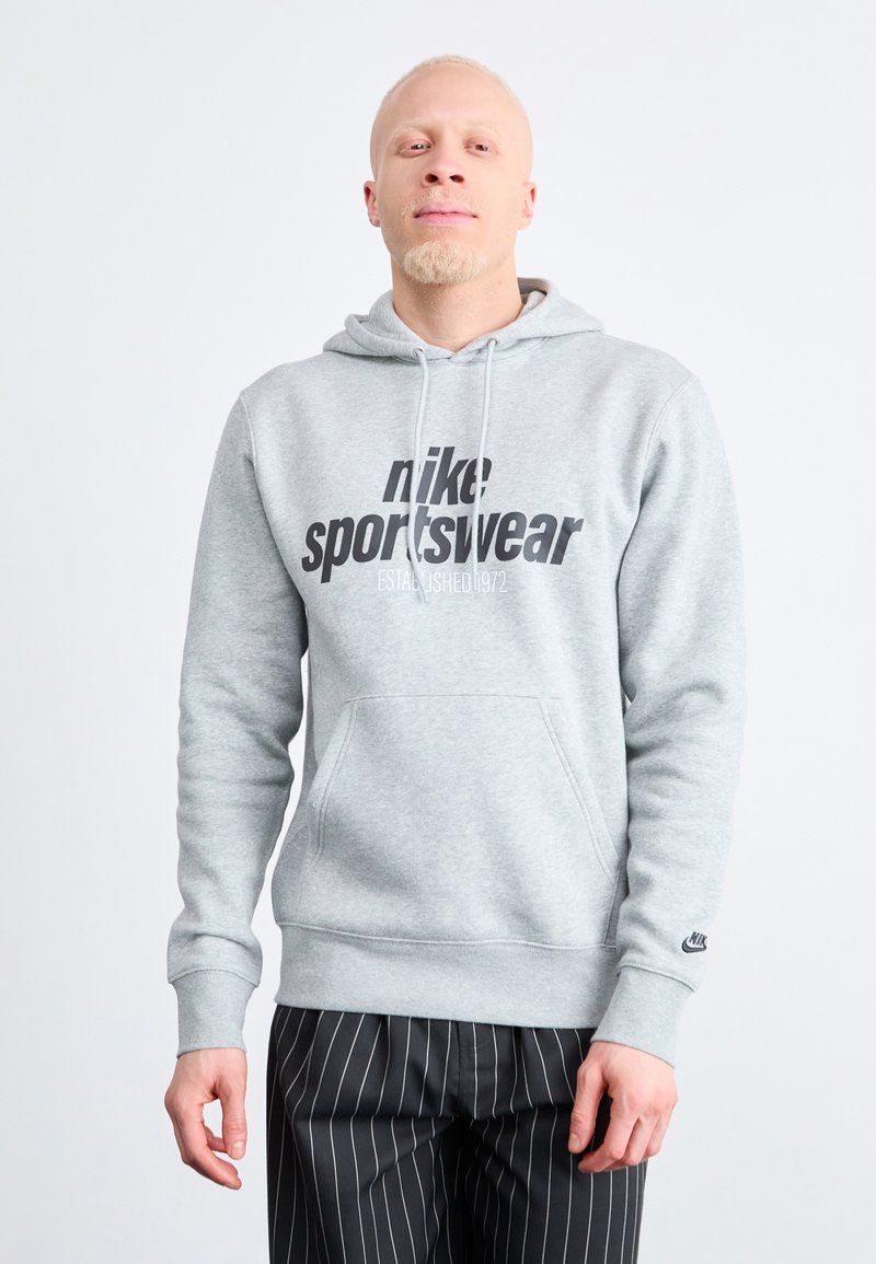 Pilkas medvilnės džemperis su dideliu juodu "nike sportswear" grafinu, su kapuce ir kengūros kišene. Rausvos rankogaliai ir apatinis kraštas.