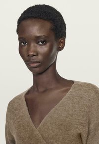 Brauner, gestrickter Pullover mit V-Ausschnitt; weicher Stoff; leichtes, luftiges Material; dezente Nahtdetails am Halsausschnitt.