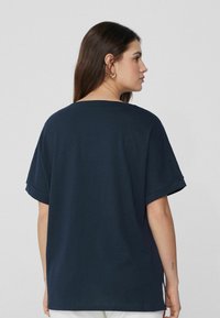 Námořnická modrá oversized tričko s krátkými ohrnutými rukávy a širokým výstřihem. Měkký bavlněný materiál s hladkou strukturou. Bez vzorů.