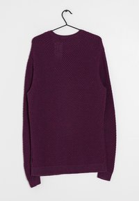 Lila stickad tröja med texturerad mönster, långa ärmar och rund halsringning. Har en rak fåll och sidofickor.