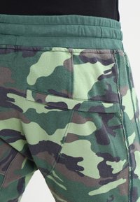 Kamouflage joggers i grön, svart och khaki. Mjuk bomullsmaterial med elastisk midja och sidofickor.