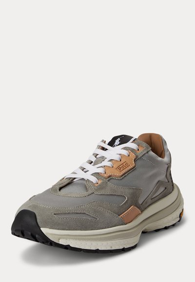 Baskets grises et beige avec lacets blancs, semelle texturée, et logo Polo sur la languette et le côté, présentées légèrement inclinées sur fond blanc.