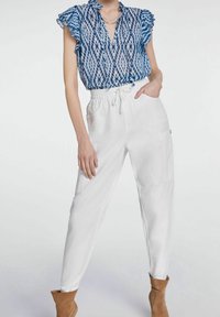 Blouse à motifs bleus et blancs avec manches à volants, associée à un pantalon blanc à taille élastique et des bottines marron. Texture de tissu lisse.