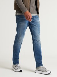 Jeans de mezclilla azules con un ajuste slim, que presentan áreas descoloridas, bolsillos estándar y un lavado claro, combinados con zapatillas deportivas grises.