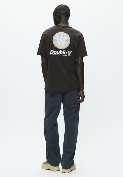 T-shirt in cotone marrone con un logo circolare con accenti blu chiaro, bianco e beige, e il testo "Double A" sul retro.