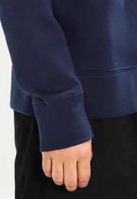 Mörkblå sweatshirt med ribbad mudd, mjuk textur och avslappnad passform, samt en synlig sömdetalj längs nederkanten.