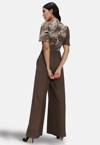 Brown jumpsuit with wide legs, short sleeves, and a patterned top in beige and brown. Features a fitted waist and smooth texture.
