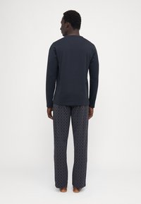 Conjunto de ropa de estar en casa para hombres que incluye una camiseta de manga larga de color azul oscuro y pantalones oscuros de rayas grises con un diseño sutil, fabricados con tela suave.