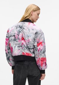 Giubbotto bomber con una stampa astratta colorata nei toni del rosa, grigio e bianco, realizzato in un materiale lucido, con polsini e orlo a coste neri.