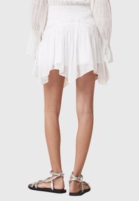 White, flowing skirt with a high-low hem and textured fabric. Pair of silver strappy sandals with a black sole and adjustable buckles.