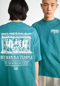 Teal cotton oversized t-shirt featuring a white graphic print of classical figures and text, with a relaxed fit and short sleeves.