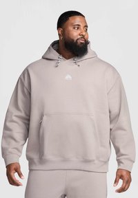 Sweat à capuche gris clair en tissu doux, doté d'une grande poche avant et d'un petit logo sur la poitrine, avec des cordons de serrage réglables.