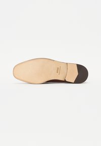 Sole di scarpa in pelle marrone con una base beige liscia, forma curvata e grip sul tallone marrone testurizzato. Nome del marchio "BOSS" impresso sulla suola.