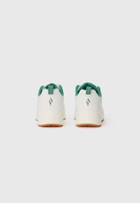 Hvite sneakers med grønn innredning og gummisåler, sett fra baksiden som viser et lite sølvlogo på hver hæl.