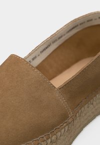 Espadrille marron en daim à enfiler avec une semelle en jute tressé et des coutures visibles le long du bord supérieur et de la semelle.