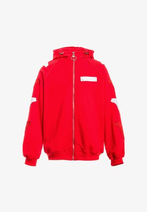 Sudadera con capucha roja y cremallera, con parches en forma de alas blancas y rojas en las mangas, capucha con cordón y un pequeño parche rectangular blanco en el pecho.
