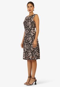 Zwarte bloemenjurk met een getailleerde silhouet, voorzien van een textuur van roze bloemmotieven. Gepaard met zwarte sandalen met bandjes met unieke accenten.