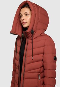 Red puffer jacket with a large, hooded collar, featuring quilted padding, a zip front, and adjustable drawstrings at the neck.
