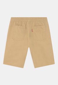 Pantaloni corti beige fino al ginocchio con vita elasticizzata e due tasche posteriori, con un piccolo tag del marchio rosso sulla tasca destra.