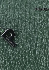 Materiale verde testurizzato con una finitura lucida, caratterizzato da un charm metallico prominente e un logo impresso, creando un motivo di forme arrotondate.