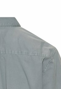 Helles graues Hemd mit Knopfleiste, das einen Kragen, eine weiche Textur und sichtbare Nähte an den Schultern und am Rücken aufweist, mit einem klaren Schnittdesign.