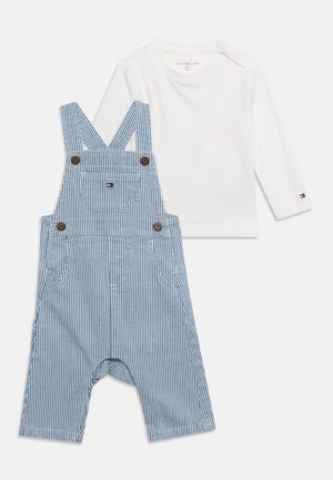 Wit babyshirt met lange mouwen en drukknoopjes op de schouders, gecombineerd met blauw-wit gestreepte baby tuinbroek met voorzak en bretels met knopen.