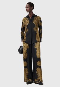 Black satin shirt and wide-leg pants featuring intricate gold paisley patterns, paired with a black handbag and flat shoes.