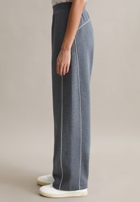 Szare spodnie dresowe o luźnym kroju, z białym paskiem po bokach i elastycznym pasem. W zestawie z białymi tenisówkami.