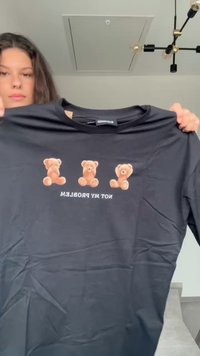 Camiseta negra con tres ositos de peluche de dibujos animados sobre el texto "NO ES MI PROBLEMA". Está hecha de una tela suave y tiene un diseño de cuello redondo.