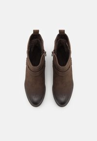 Hnědé kotníkové boty s hladkým svrškem, kulatou špičkou a kontrastní tmavou špičkou. Detail zipu na boku a měkké vnitřní podšívání.