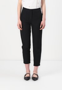 Zwarte, taps toelopende broek met een gladde textuur, voorzien van een hoge tailleband en een cropped lengte, gecombineerd met zwarte ballerina's versierd met metalen accenten.