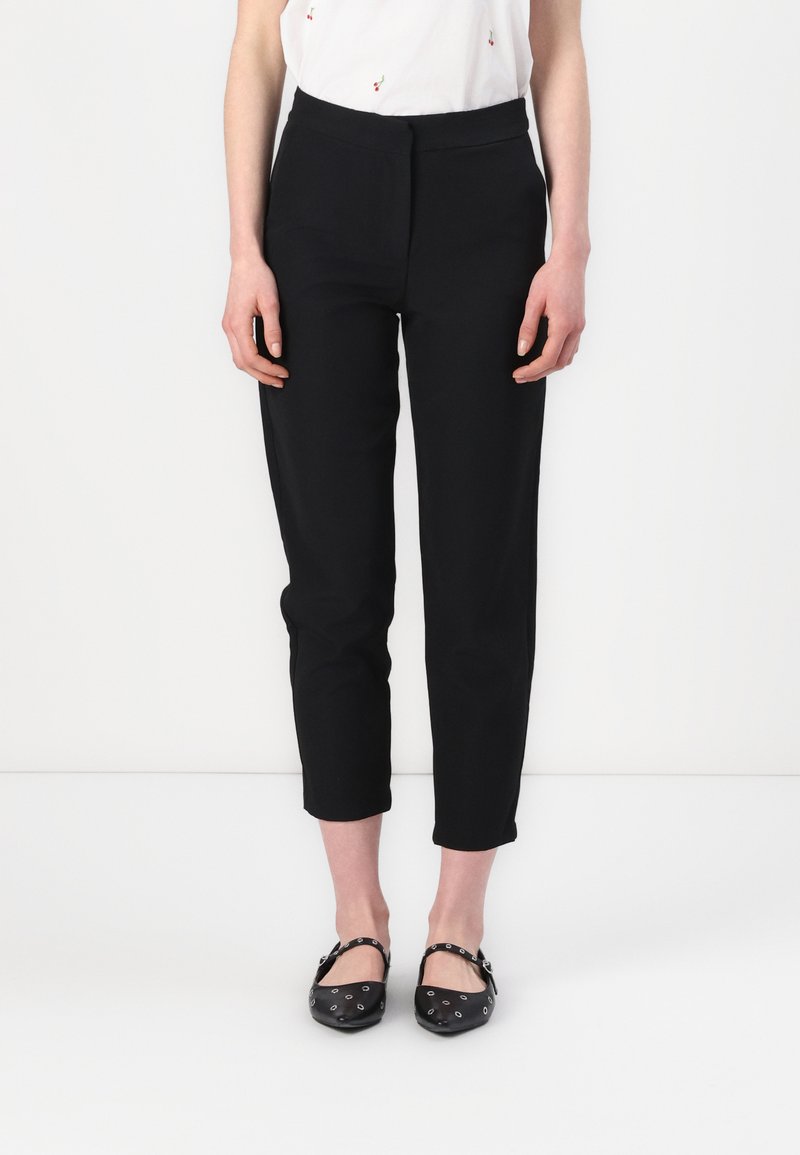 Zwarte, taps toelopende broek met een gladde textuur, voorzien van een hoge tailleband en een cropped lengte, gecombineerd met zwarte ballerina's versierd met metalen accenten.