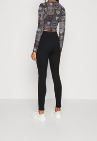 Zwarte mesh top met lange mouwen en hartpatronen, gecombineerd met hoge zwarte leggings en lichtgekleurde sneakers.