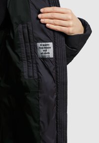 Black insulated jacket interior featuring a stitched texture and a label reading "A warm hug made out of cloth." Smooth fabric.
