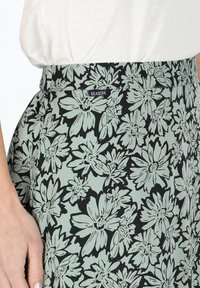 Jupe fleurie avec un fond noir, ornée de fleurs vert clair dans un style esquissé. Comprend une étiquette "SEASIDE" sur la taille.