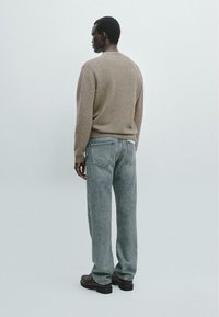 Maglione di lana beige con scollatura rotonda abbinato a pantaloni in denim grigio chiaro e scarpe in pelle nere, visto da dietro.