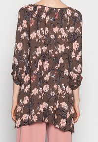 Brun blomsterbluse med trekvartærmer. Har rosa og hvite blomstermønstre, bløt tekstur og et løst, svakt design.
