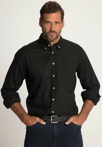 Camisa negra de botones con cuello, de mangas largas remangadas en los puños y un bolsillo en el pecho. Presenta botones blancos y una textura suave.
