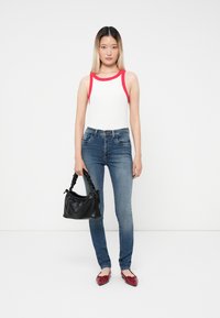 Top blanco sin mangas con ribete rojo, pantalones ajustados azules, zapatos planos rojos y un pequeño bolso negro con asa arrugada. Texturas suaves y diseño ajustado.