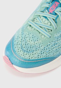 Baskets turqueses avec une tige en mesh, des accents bleus et une semelle rose. Les lacets sont plats avec un motif texturé.