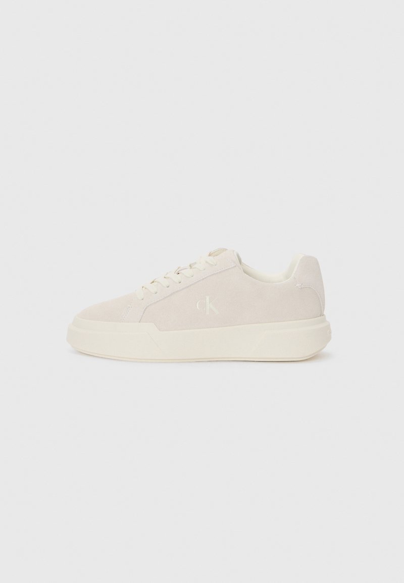 Lys beige semsket sneakers med en tykk kremfarget såle, rund tå, snøring foran og subtil logo detalj på siden. Klassisk lavt topp design.