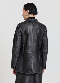 Blazer in pelle nera con vestibilità strutturata e dettagli di cuciture visibili, caratterizzato da un colletto a revers e una texture liscia opaca.