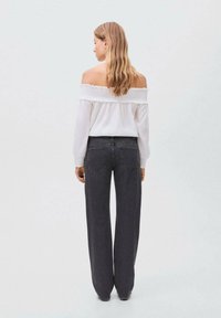 Blusa bianca off-the-shoulder in tessuto testurizzato con maniche lunghe, abbinata a jeans grigio scuro a vita alta e a gamba larga con tasche posteriori.