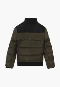 Puffer jacket featuring a dark olive green quilted body, black shoulder panel, and ribbed black cuffs and hem. Textured material and structured design.