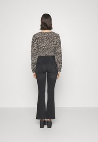 Top med leopardmönster och långa ärmar, tillsammans med högmidjade svarta utsvängda jeans. Tjocka svarta platåklackar fulländar outfiten.