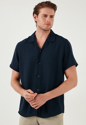 Marineblauw overhemd met korte mouwen en een plat kraagje; gestructureerde stof met subtiele glans; knopen aan de voorkant en een ontspannen pasvorm.