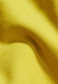 Geel stof met een zachte textuur, met een soepele, gelijkmatige weving. Het materiaal heeft een levendige kleur en een subtiele glans, wat diepte creëert in de plooien.