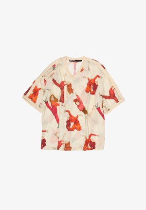 Bēša V-veida kakla īsām piedurknēm krekls ar visaptverošu sieviešu attēlu sarkanās un oranžās krāsās dažādās dinamiski dejojošās pozās.