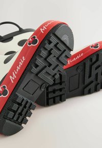 Schwarze Gummisohle mit strukturiertem Grip, roter Außenrand mit "Minnie"-Text, schwarz-weißer Polka-Dot-Design, klassische Form.