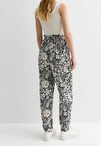 Mustat ja valkoiset kukkakuosiset housut, joissa on joustovyötärö, kapenevat lahkeet ja nilkkaremmithan, yhdistettynä valkoisiin lenkkareihin.